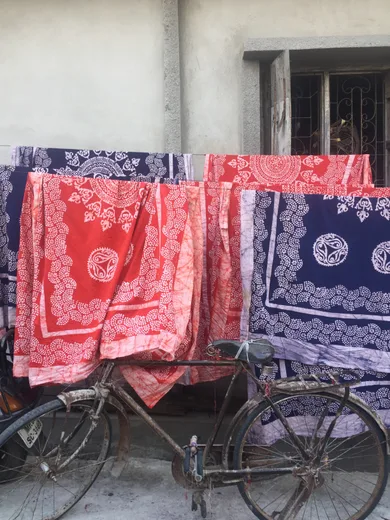 Red and indigo bandhani fabrics drying beside an old bicycle