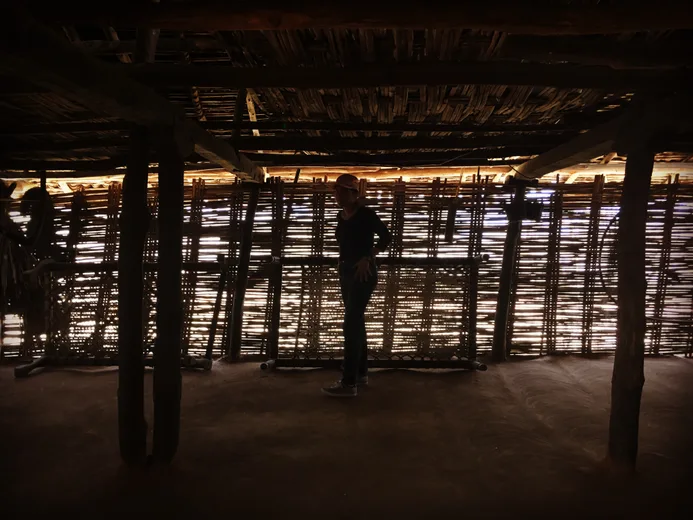 A weaver's silhouette inside a sunlit bamboo-walled workshop