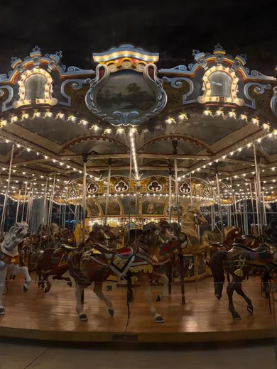 A brightly lit carousel with painted horses at night