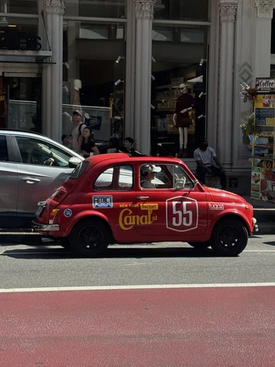 A small red vintage car numbered 55 parked on a city street