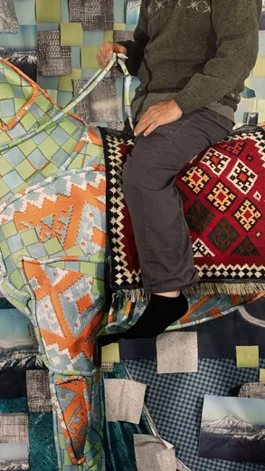 A person seated on a patchwork of colourful rugs and textiles