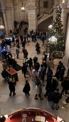 A crowd below a Christmas tree in a grand hall, seen from above