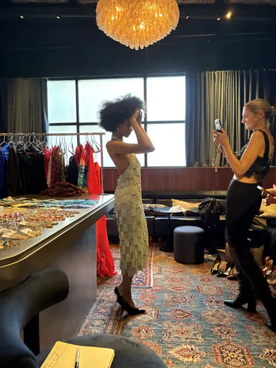 Two women at a boutique under a chandelier, one photographing the other