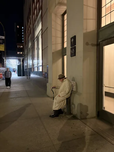 A person in a white coat sitting on a sidewalk at night