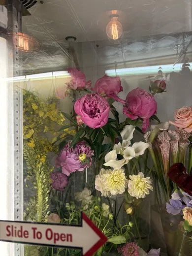 A flower shop window with peonies, lilies and a 'Slide to Open' sign