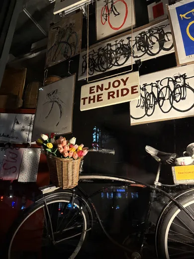 A bicycle shop wall with vintage signs, tulips in a basket and an 'Enjoy the ride' sign