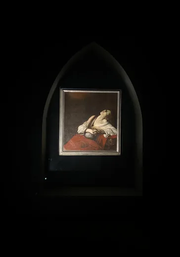 A framed painting lit in a dark, arched gallery niche