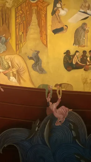 A yellow and orange mural of figures above blue waves